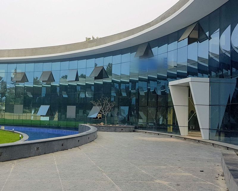 The finished building: a curved glass façade and entrance behind a paved forecourt and water channel